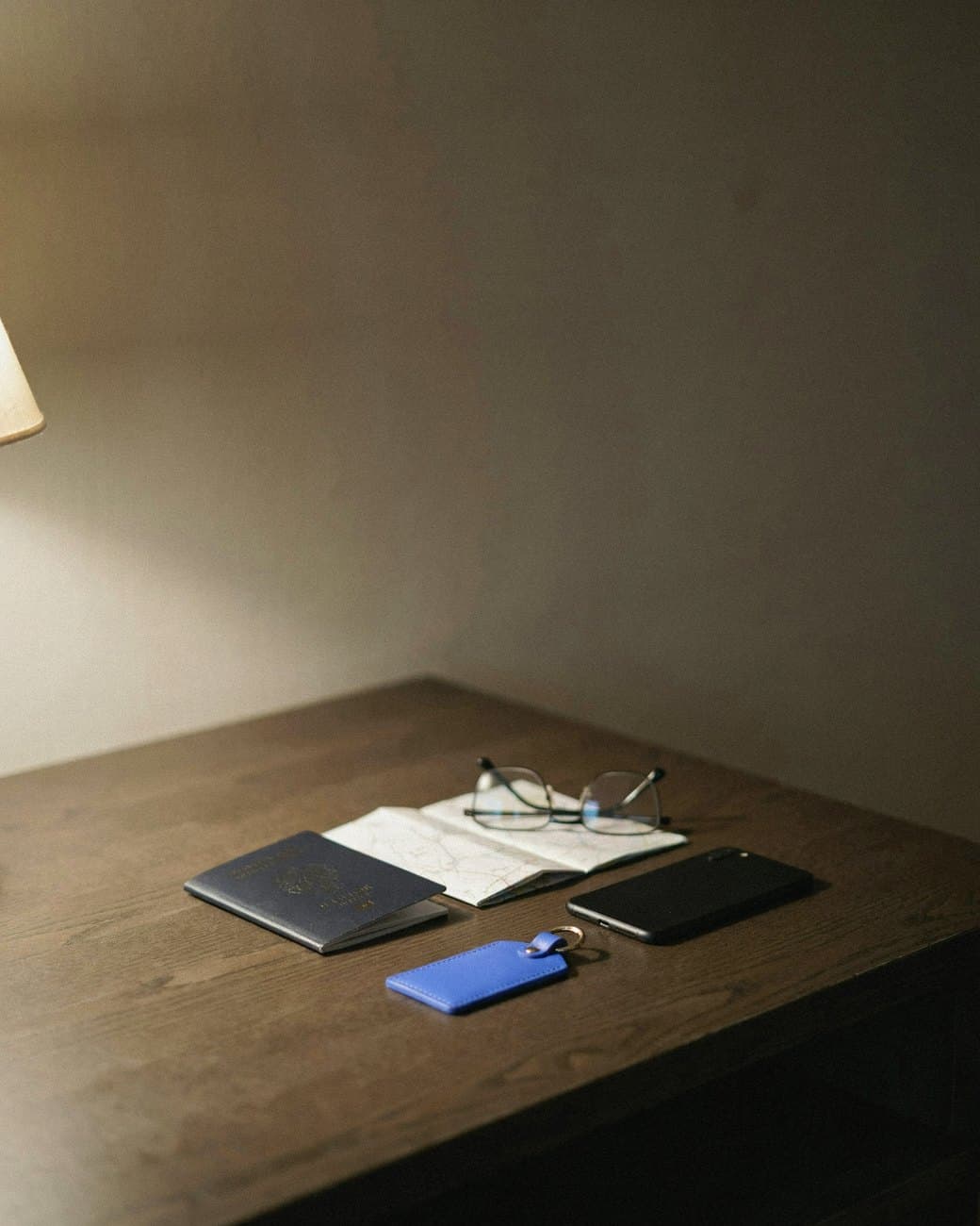 A traveller’s table at night: passport, folded map, reading glasses and a blue leather luggage tag